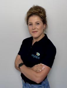 Dietetyczka Dominika Mróz w granatowej koszulce z logo Centrum Terapii Wyspa, stojąca z założonymi rękami na jasnym tle – profesjonalne zdjęcie portretowe